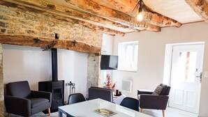Ett mysigt vardagsrum med synliga träbjälkar, en öppen spis, bekväma sittplatser och en tv.