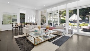 A spacious living room with a large glass coffee table, white sofas, and a dining area with chairs.