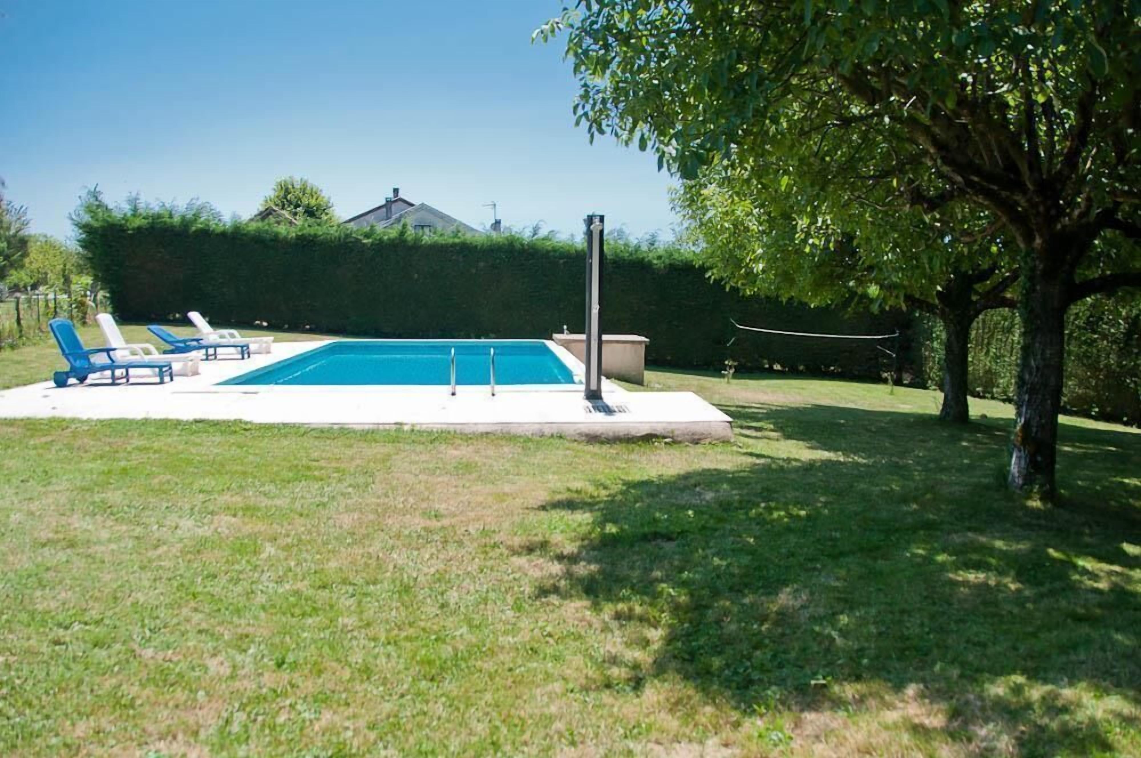 Une piscine rectangulaire dotée d’une plage blanche, entourée d’une pelouse verdoyante et d’une haie.