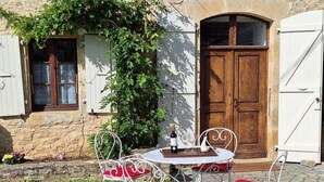 Un edificio de piedra con puerta de madera, una verja blanca y una pequeña mesa con sillas en el exterior.