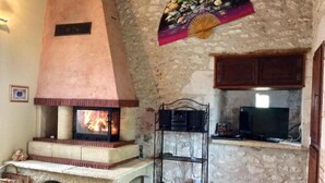 Una stanza con pareti in pietra, un caminetto, una televisione e uno scaffale con utensili da cucina.