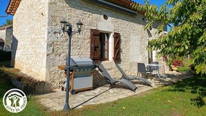 Un edificio in pietra con tetto in tegole, un barbecue e posti a sedere all'aperto.