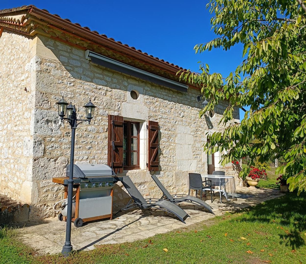 Un bâtiment en pierre avec un toit en tuiles, un barbecue et des sièges à l’extérieur.