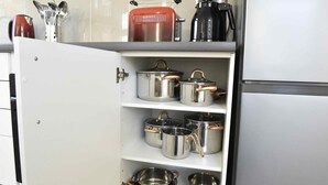 A kitchen cabinet with stainless steel pots and pans, a red kettle, and a coffee maker. - Fewo Wuppertal (Wuppertal)