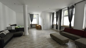A spacious living room with a large window, a sofa, a coffee table, and a dining area. - Fewo Wuppertal (Wuppertal)