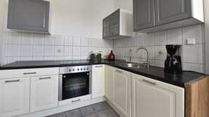 A modern kitchen with white cabinets, a black countertop, a built-in oven, a coffee maker, and a stainless steel sink. - Fewo Wuppertal (Wuppertal)
