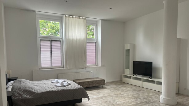 A modern bedroom with a bed, bench, TV, and windows. - Fewo Wuppertal (Wuppertal)