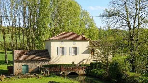 Un bâtiment à deux étages, avec un toit recouvert de tuiles rouges, un petit pont et un canal en face.