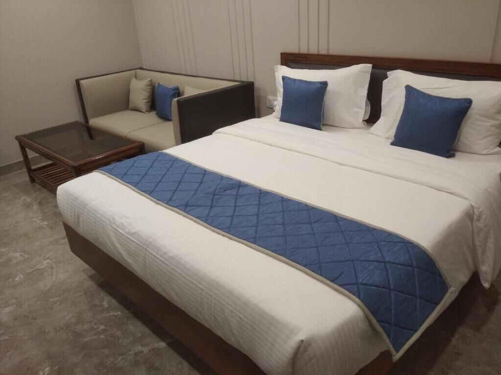 A hotel room with a large bed, a sofa, a small table, and a nightstand.