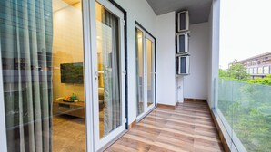 Un balcón con piso de madera, puertas de vidrio y vista a zonas verdes.