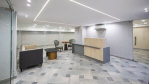 Un área de recepción moderna con mostrador, zona de estar con sofás y sillones, y suelo estampado.