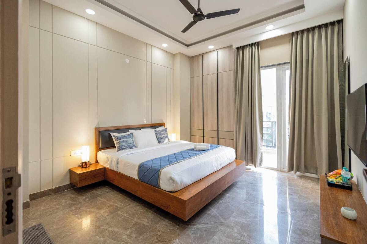 A modern hotel room with a large bed, a ceiling fan, a TV, and a view of the outdoors.