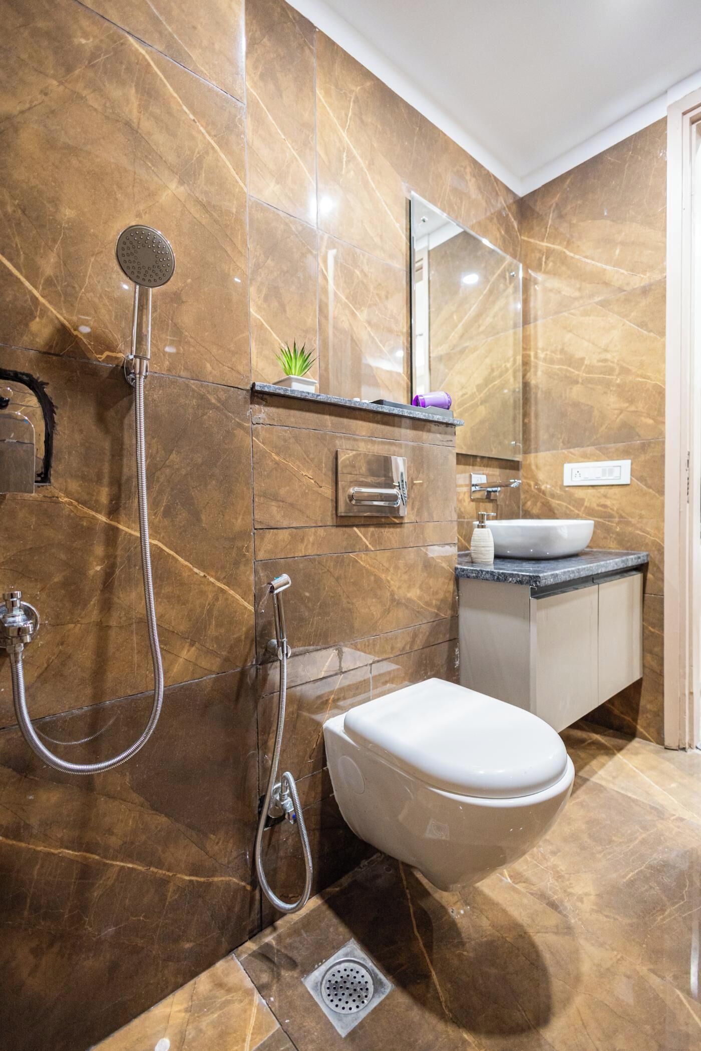 A bathroom with a marble floor, a white toilet, a sink with a marble countertop, and a shower with a handheld showerhead.