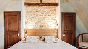 A bedroom with a stone wall, wooden headboard, and two doors. - Gite de la Bouysse Haute (CUZANCE)