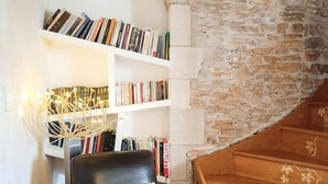 A cozy room with a stone wall, a wooden staircase, a leather armchair, and a bookshelf filled with books. - Gite de la Bouysse Haute (CUZANCE)