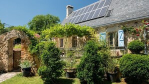 A stone house with a garden, solar panels, and a stone archway. - Gite de la Bouysse Haute (CUZANCE)