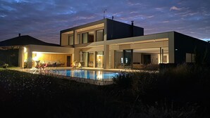 Een modern huis met twee verdiepingen, een zwembad, grote ramen en een goed verlicht terras.