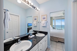 A bathroom with two sinks, a mirror, and a bed with a view.