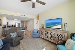A living room with a television, seating, and a kitchen in the background.