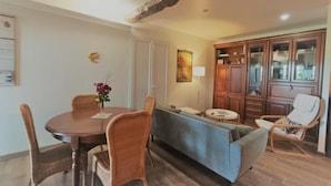 A dining area with a wooden table and wicker chairs, a blue sofa, and a wooden cabinet with glass doors. - Gîtes de France® - La Quercynoise (BERGANTY)