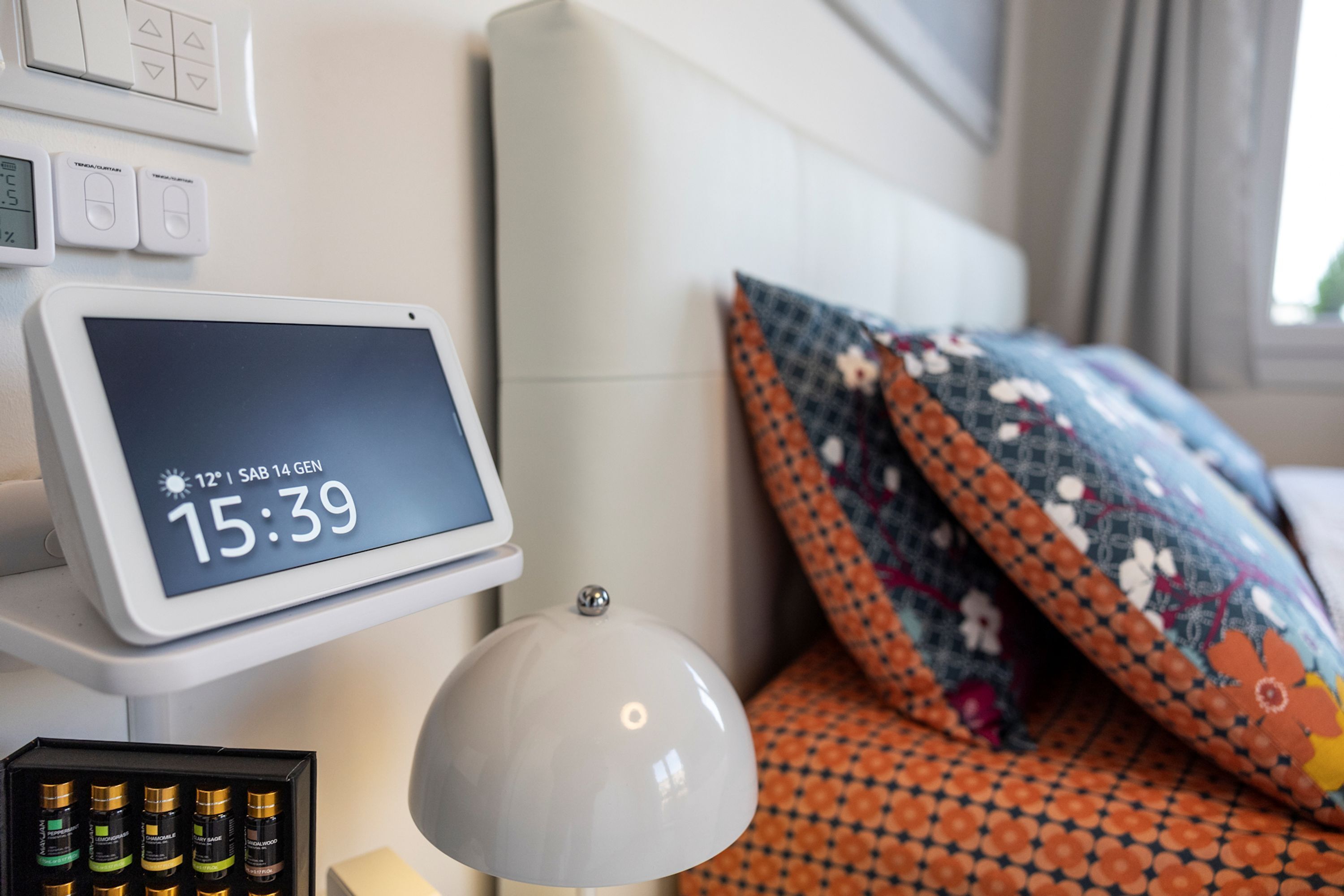 A bedside table with a digital clock, a lamp, and a box of toiletries.