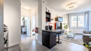 Et moderne køkken med en central ø, et spiseområde med et glasbord, og en stue med sofa og stort vindue.