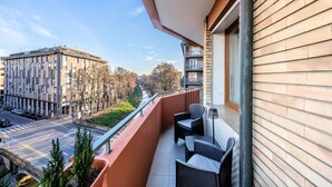 En balkon med fletmøbler, udsigt til en bygade og en bygning i baggrunden.