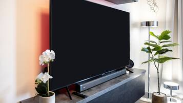A modern living room with a flat-screen TV mounted on a dark console, a potted orchid, and a tall plant beside a floor lamp.