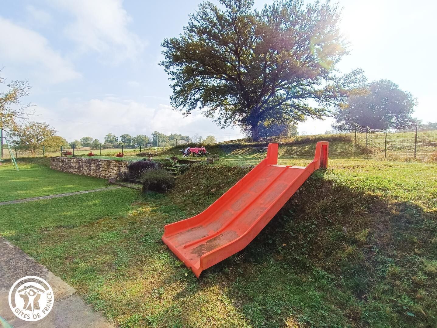 A playground with a red slide, surrounded by grass and trees.