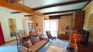 Una sala de estar acogedora con un sofá, una mesa de comedor con sillas, una zona de cocina con estufa y una pared de piedra.