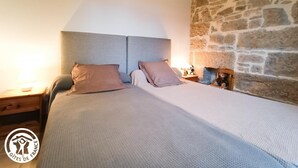 Ein Schlafzimmer mit Steinwand, einem Bett mit zwei Kissen, einem Nachttisch mit Lampe und einem kleinen Tisch mit einer Uhr.