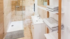 Une salle de bain moderne avec une douche à parois de verre, un lavabo blanc et une étagère en bois où sont posées des serviettes.