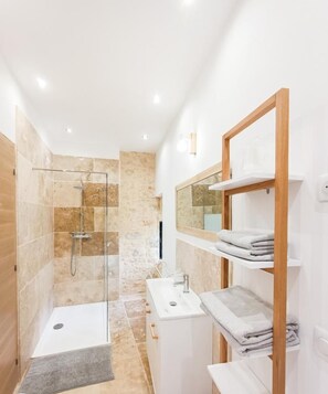 A modern bathroom with a glass-enclosed shower, a white sink, and a wooden shelf with towels.