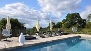 A swimming pool with lounge chairs and umbrellas, surrounded by a fence and trees. - Gîtes de France® - La Maison de Campagne (ALVIGNAC)