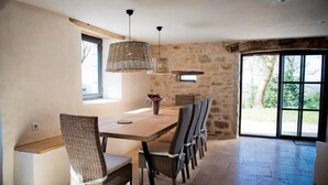 A dining area with a long wooden table, wicker chairs, and hanging light fixtures. - Gîtes de France® - La Maison de Campagne (ALVIGNAC)