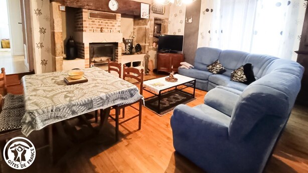 Una sala de estar acogedora con un sofá azul, una mesa de comedor con mantel estampado, una chimenea y un televisor.