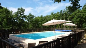 Una piscina rectangular con terraza de madera y sillas de descanso.