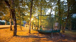 Un trampolín en un área boscosa con árboles y una casa al fondo.