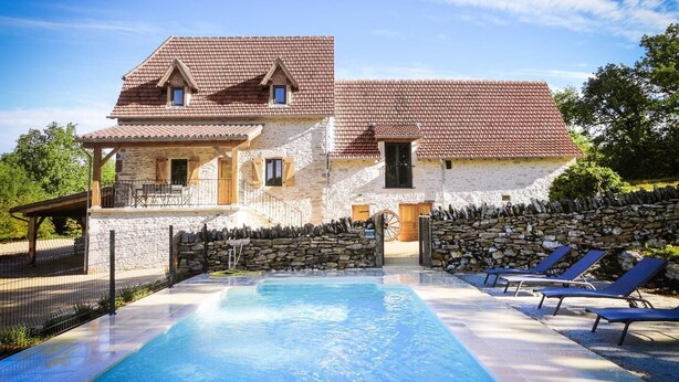 A two-story stone house with a swimming pool and lounge chairs.