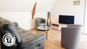 A modern living room with a leather sofa, a grey armchair, a glass coffee table, and a flat-screen TV.