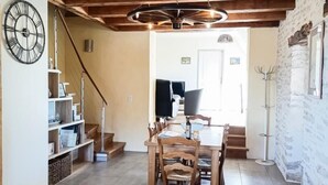 A dining area with a wooden table and chairs, a clock on the wall, and a staircase leading to another room.