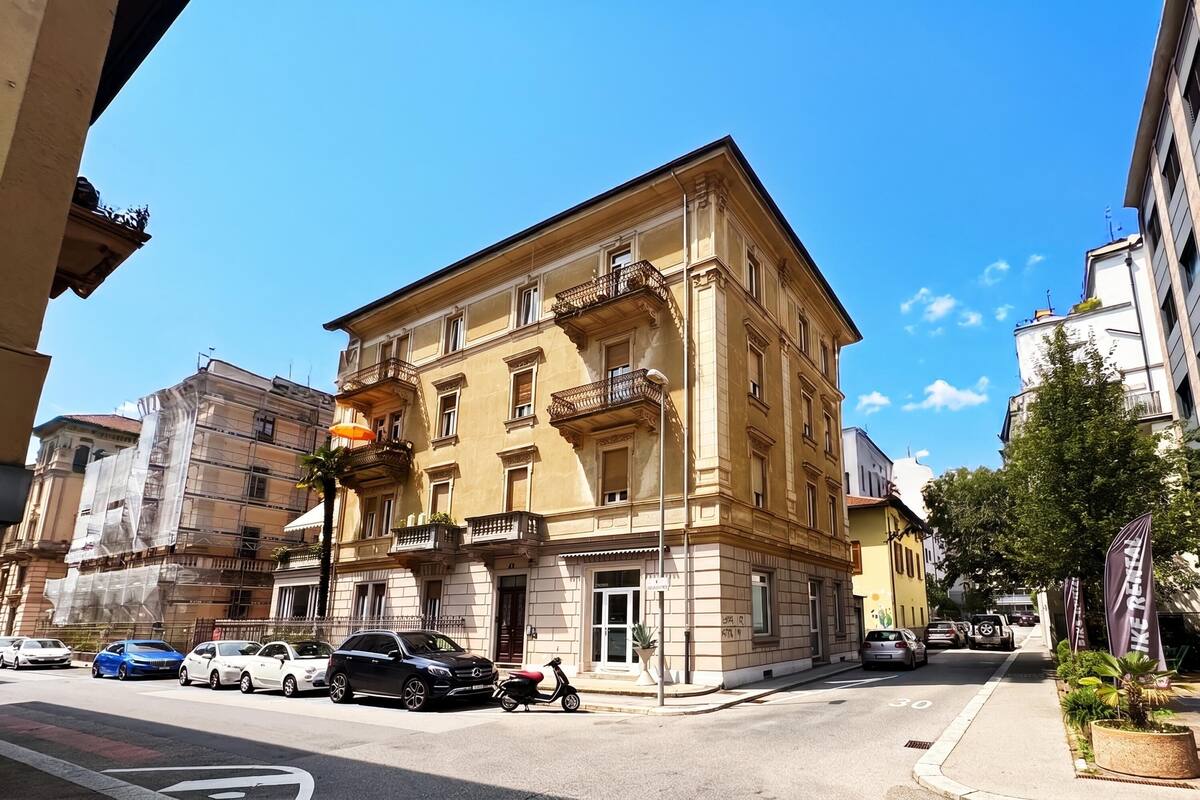 A multi-story building with balconies, parked cars, and a clear sky.