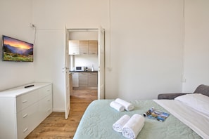 Une chambre à coucher avec un lit, un bureau, une chaise, un tableau et une vue sur la cuisine.