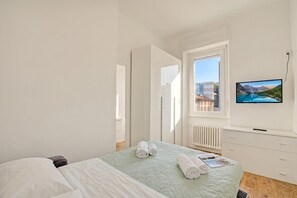 A bedroom with a bed, a TV, a window with a view, and a radiator. - Via Canonica Apartments (Lugano)