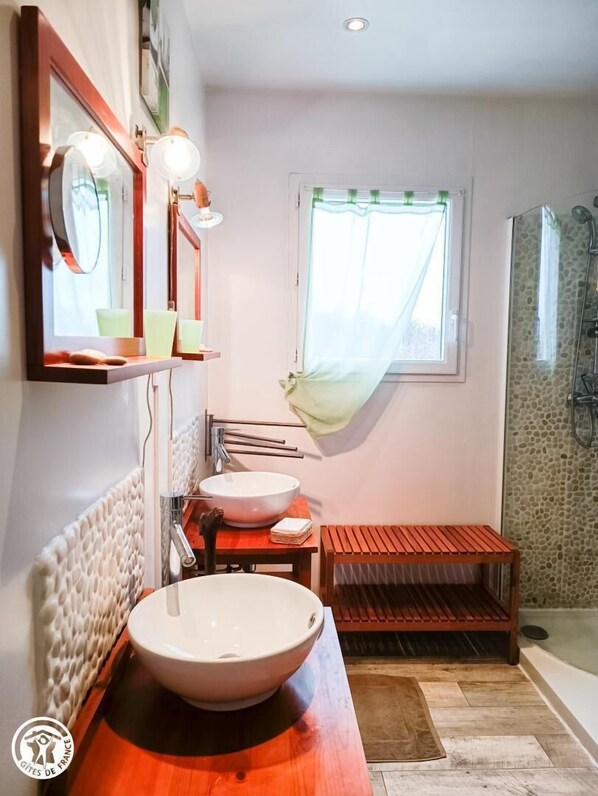 A bathroom with a large basin, a mirror, a window with a curtain, and a shower area.