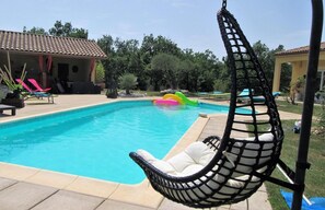 A swimming pool with a hanging chair, lounge chairs, and a small slide.