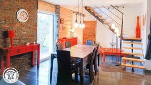 Et moderne spiseområde med et træbord, stole og et rødt skab. En trappe med trætrapper og en rød vase er synlig i baggrunden.