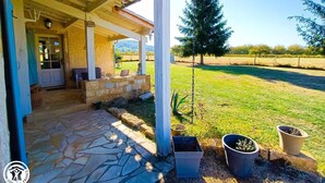 Eine überdachte Terrasse mit Steinboden, Sitzgelegenheiten im Freien und Topfpflanzen.