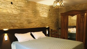 Ein Schlafzimmer mit Steinwand, einem Bett mit weißer Bettwäsche, einem Holzschrank und einer Wandleuchte.