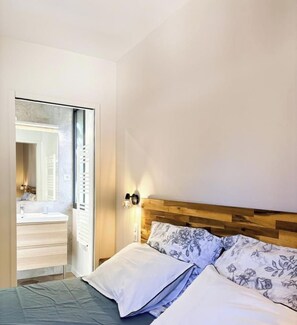Un dormitorio con cabecera de madera, cama con ropa de cama floral, mesita de noche y aplique de pared.